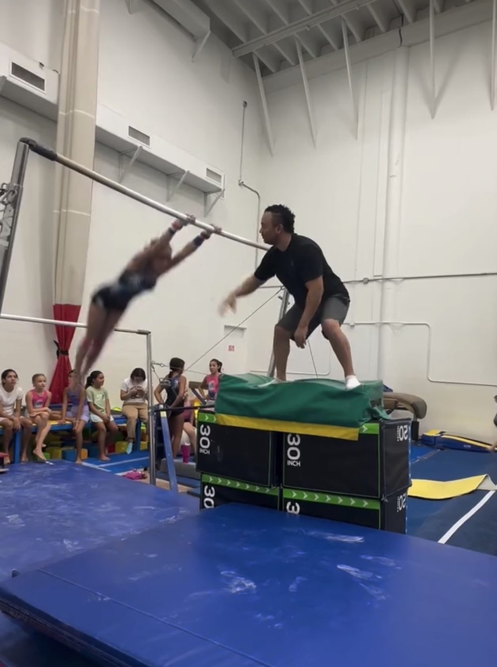 Coach José Fuentes spotting a gymnast on the high bar during a private lesson
