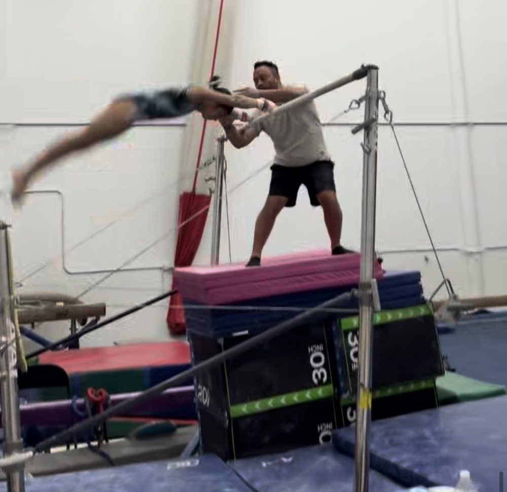 Coach Fuentes guiding a gymnast through a bar release