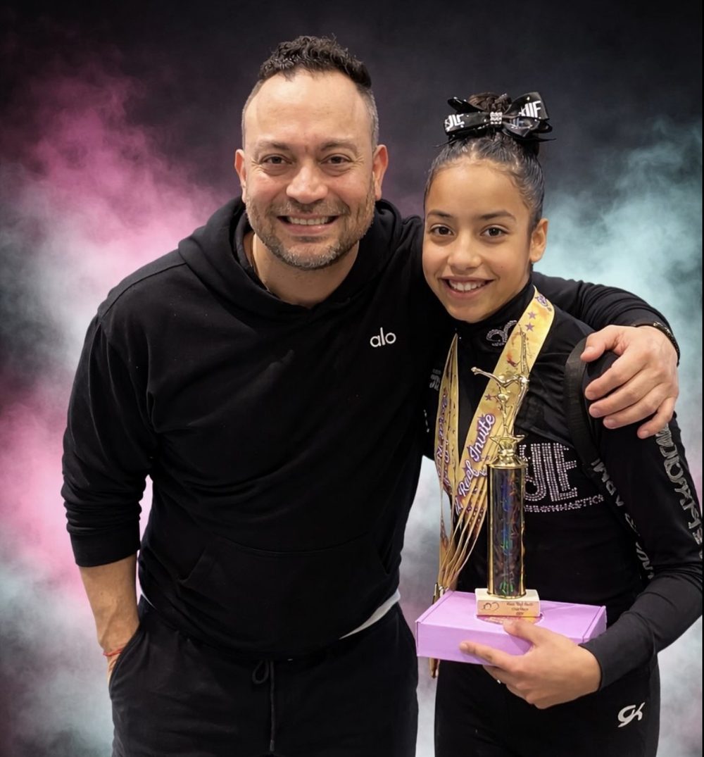 Head Coach José Luis Fuentes with a JLF Elite gymnast holding her first-place trophy and medals