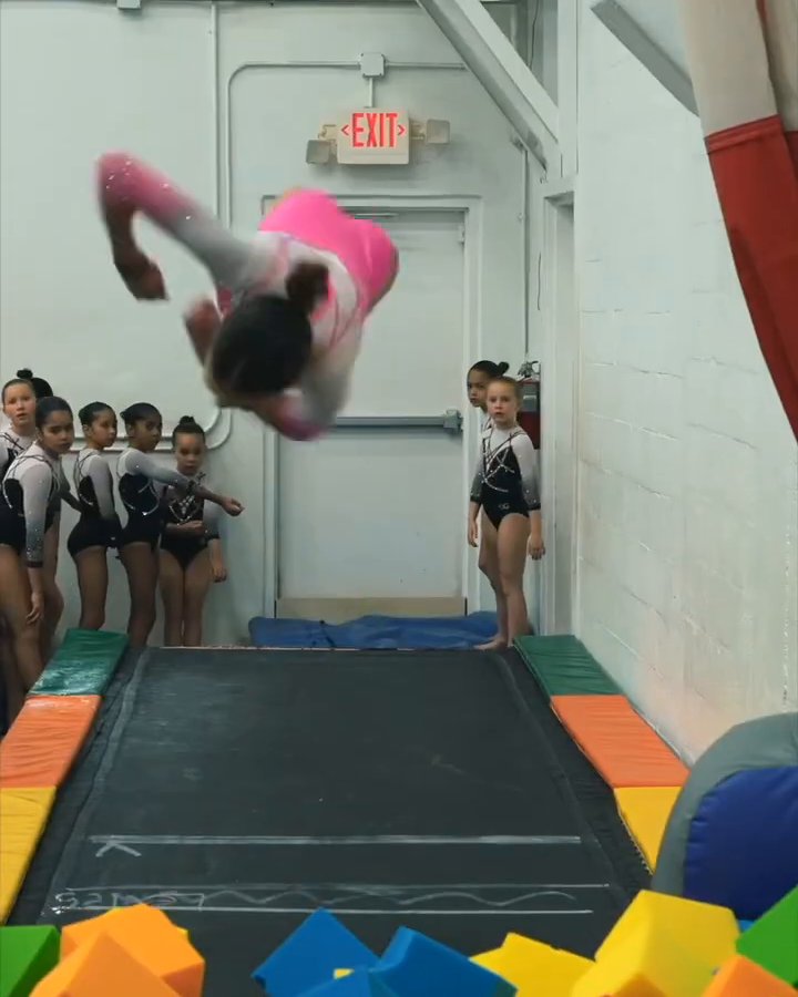 A gymnast flipping off the trampoline into the foam pit while friends watch